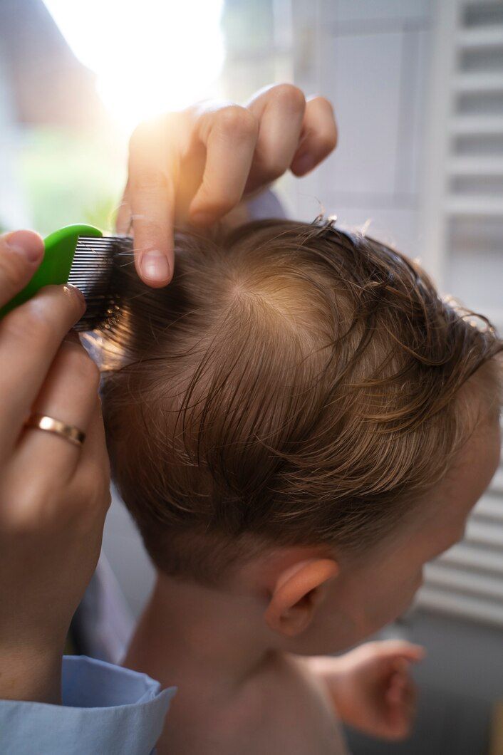 Una persona peina el cabello castaño de un niño con un peine verde cerca de una ventana.