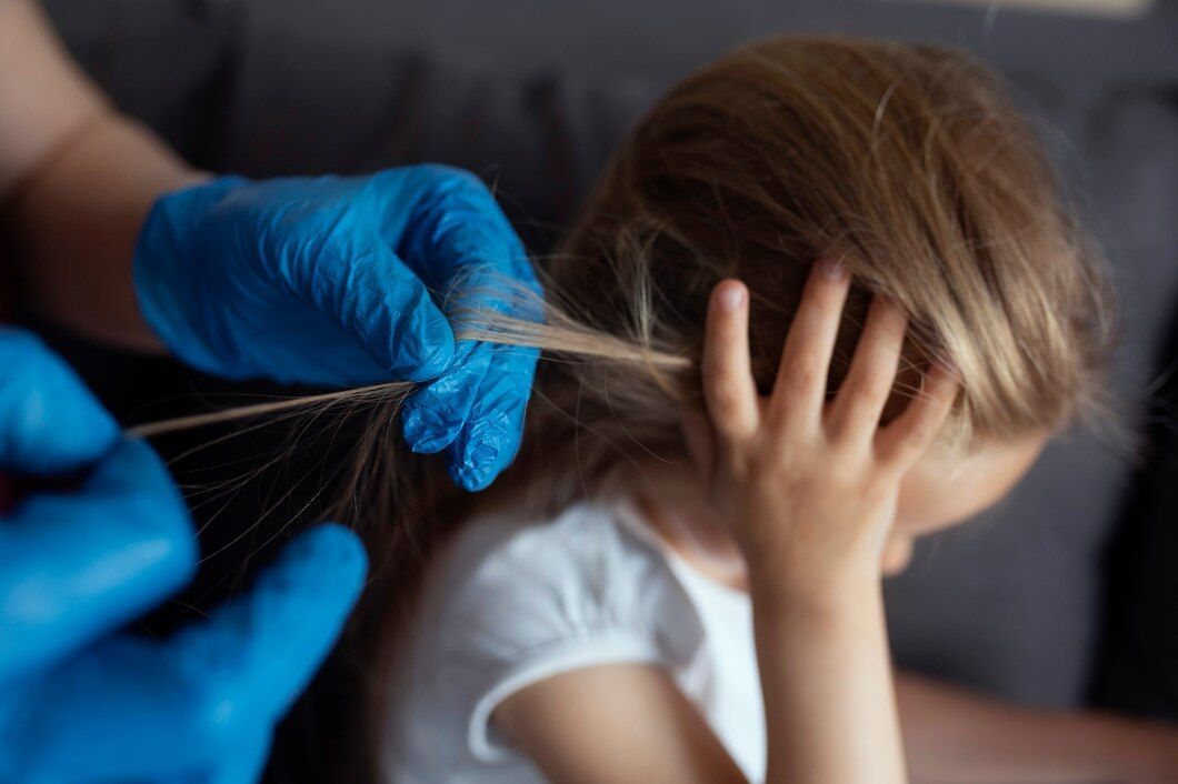 Manos enguantadas peinando el cabello castaño de un niño mientras este sostiene su cabeza en una sala de estar.