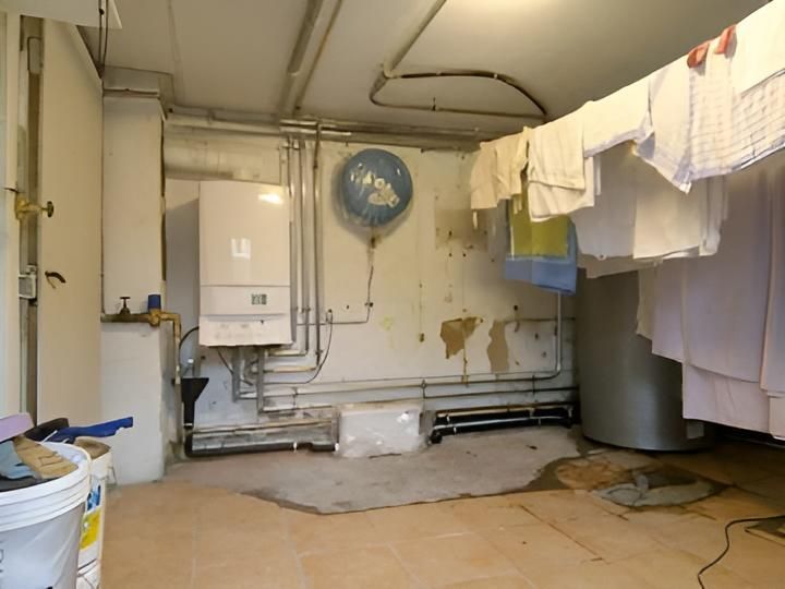 Kleiner Waschraum mit Boiler, Rohren, Wäscheleine und Wandventilator.