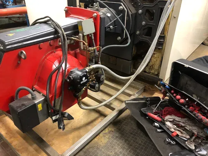 Rote mechanische Teile und Schläuche auf einer Werkbank neben einem offenen Motorraum