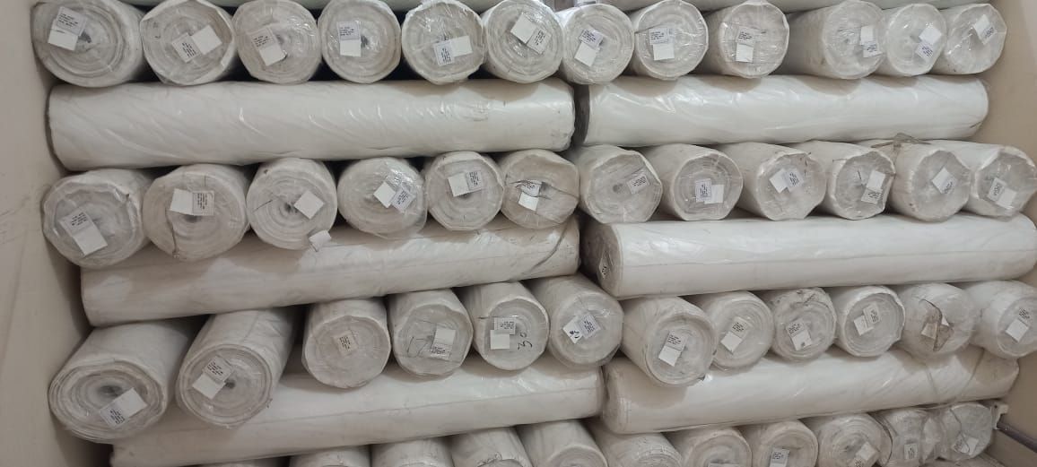 Stapel aus weißem Stoff in Rollenform in einem Lagerbehälter.