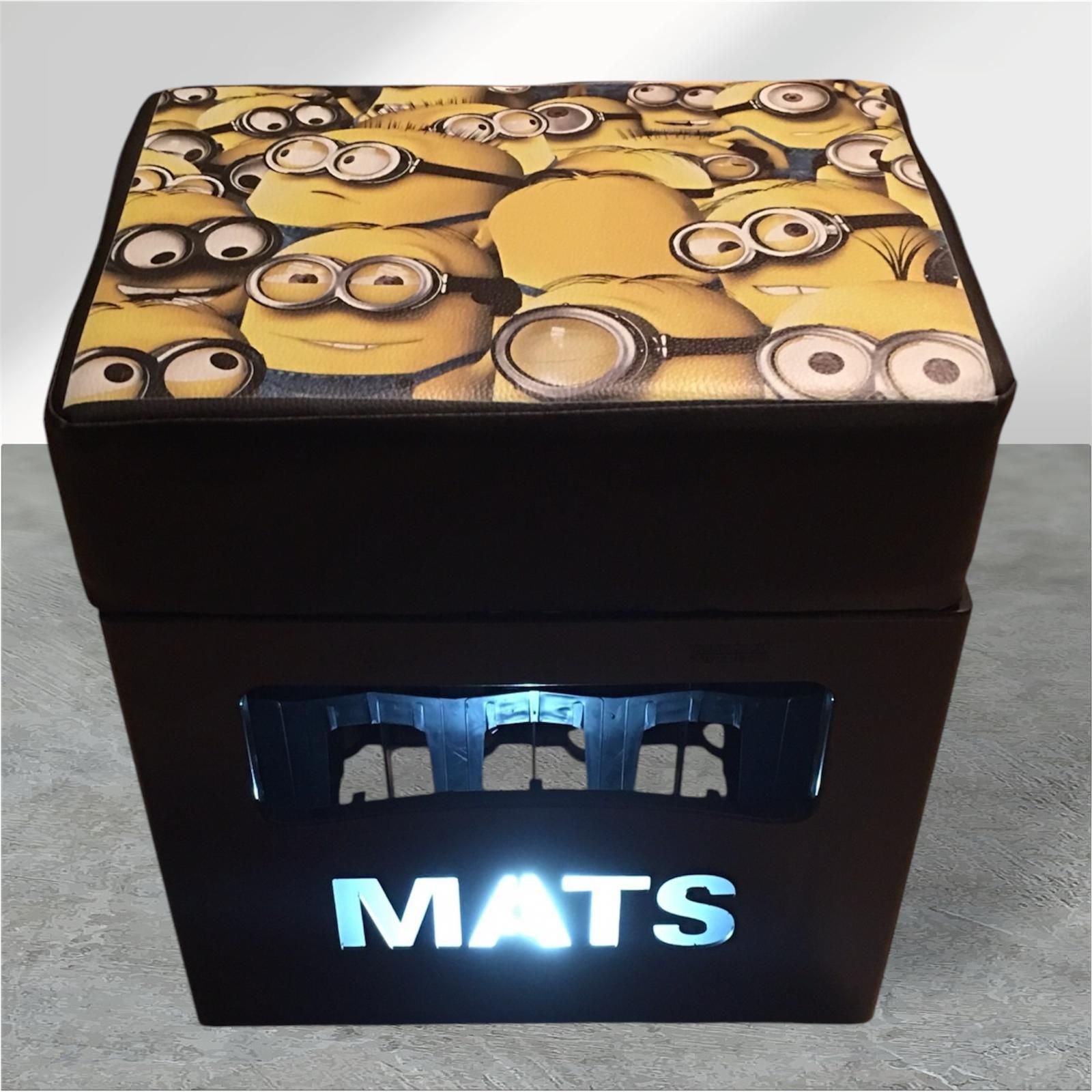 Schwarzer Ottoman mit Stauraum und Minions-Oberteil, „MATS“ beleuchtet.