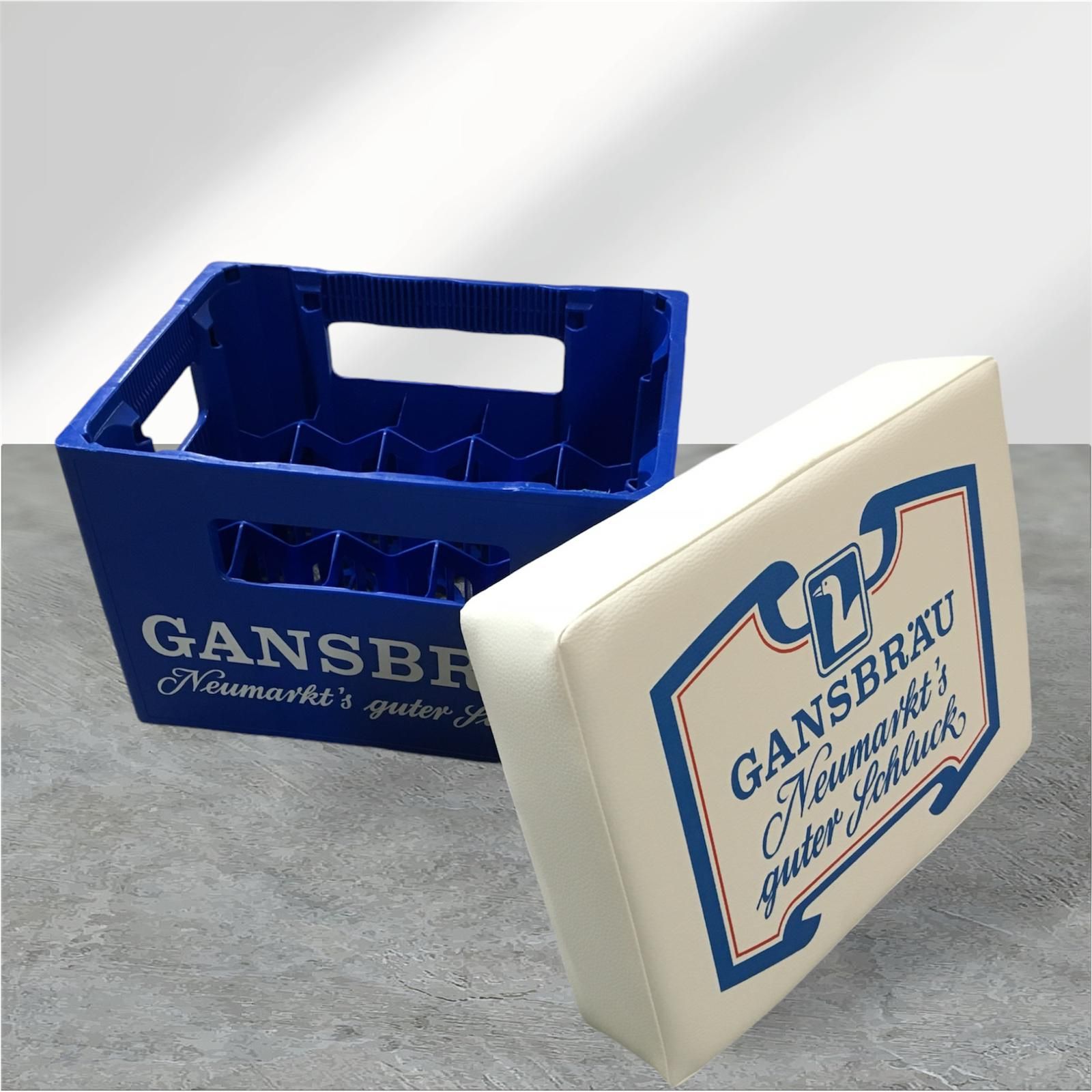 Blauer „Gansbräu“-Bierkasten mit weißem Kissen und Markenlogo.