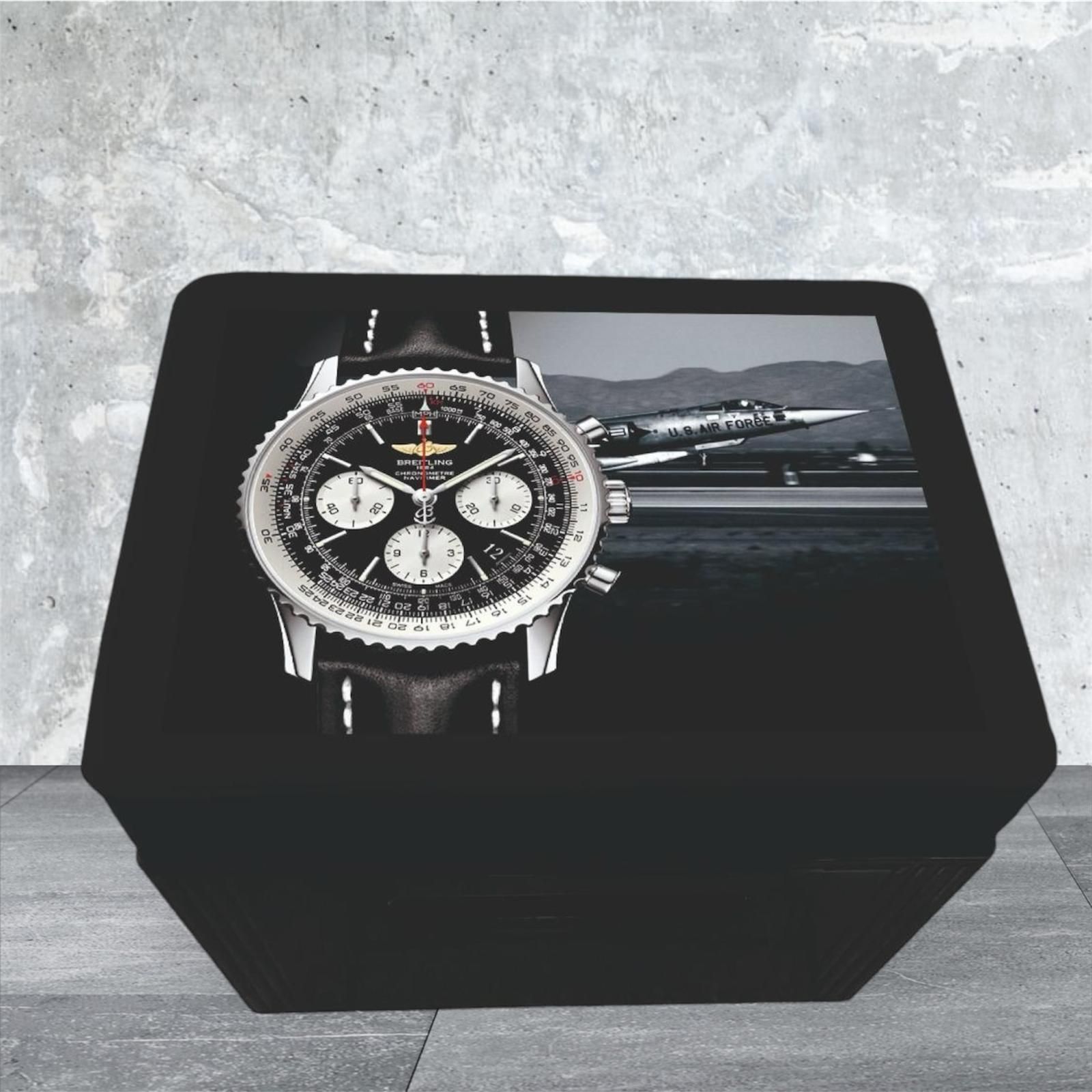 Schwarz-silberne Breitling-Uhr in einer schwarzen Vitrine mit dem Foto eines startenden Jets.