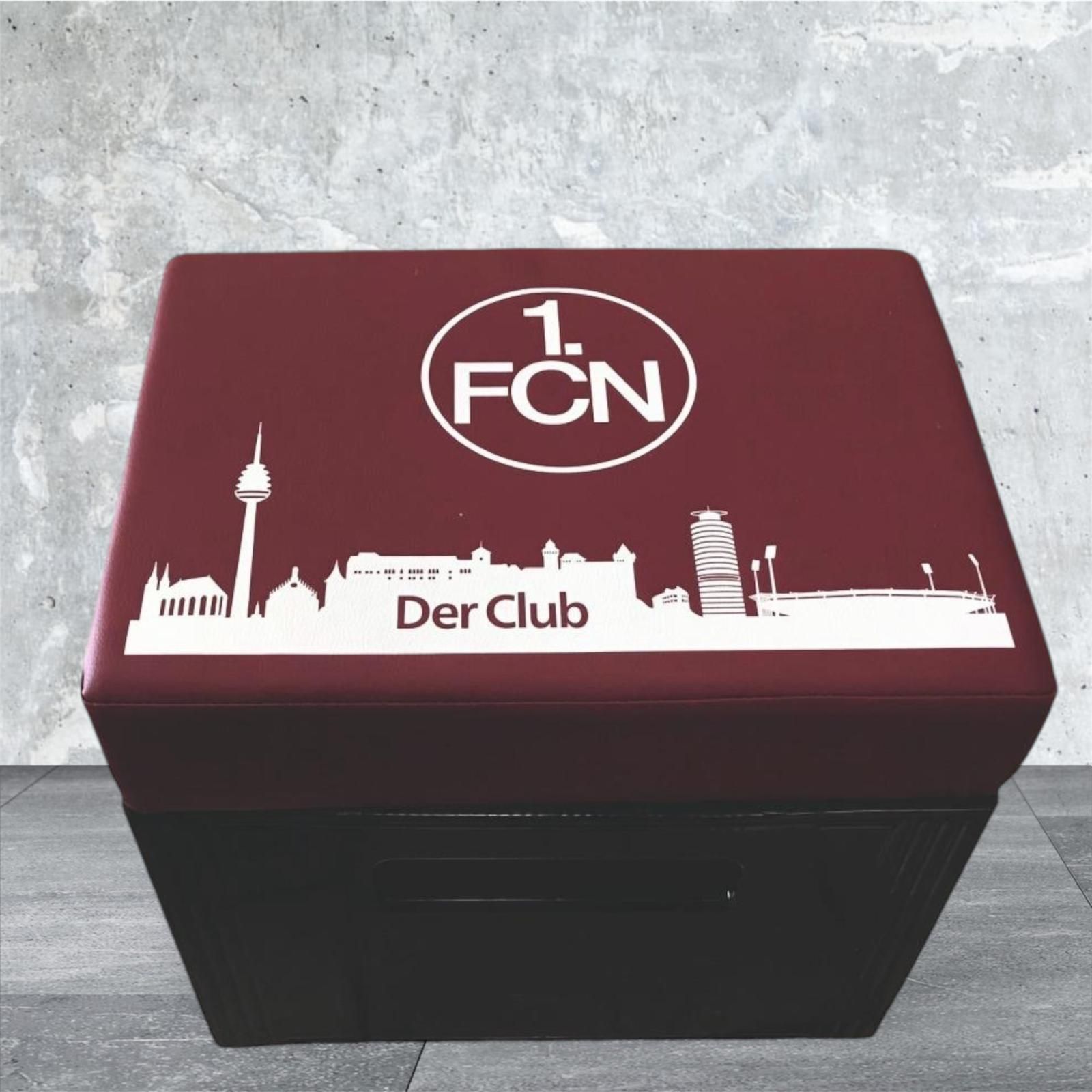 Weinrote und schwarze Sitzbank mit 1. FCN-Logo und Stadtsilhouette.