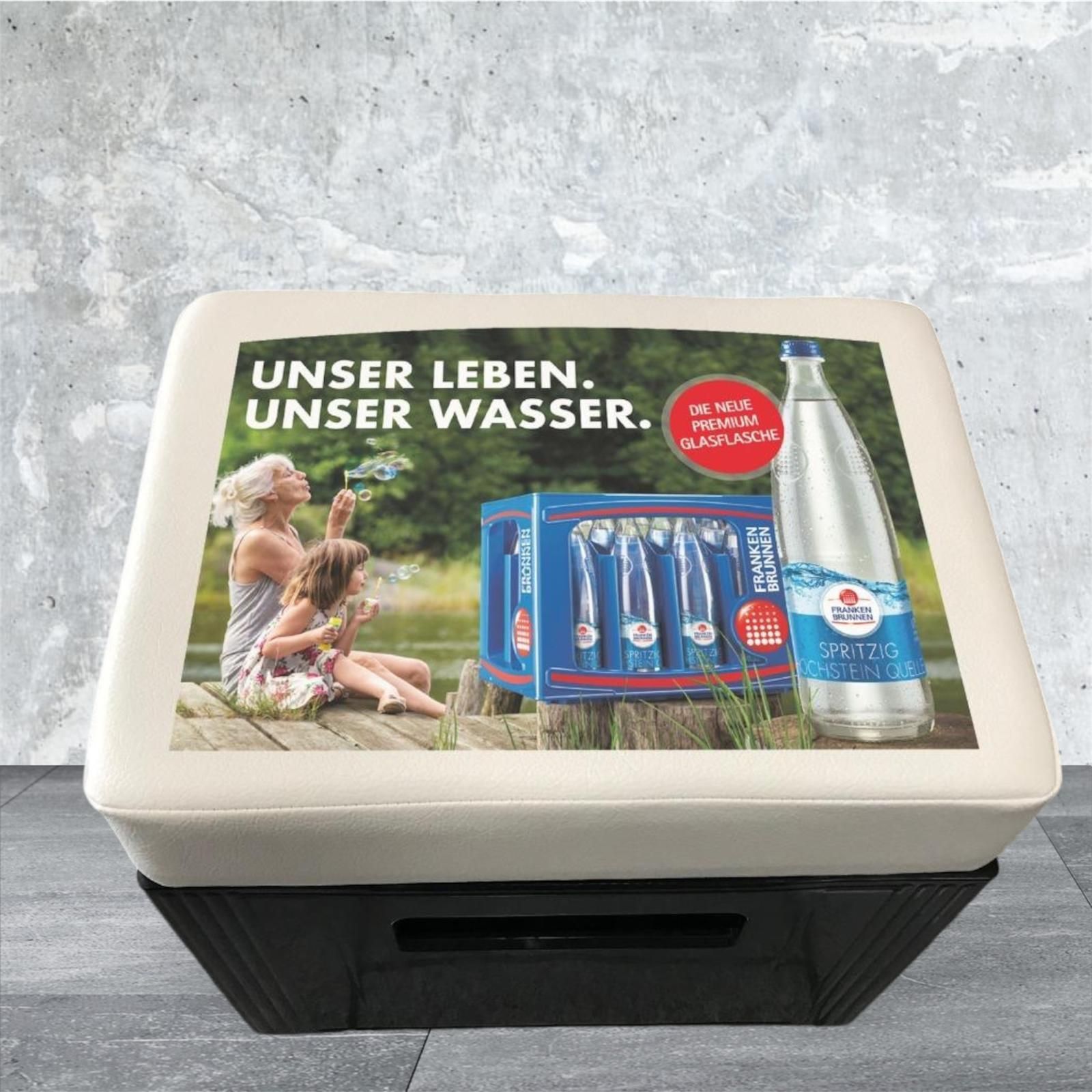 Vitrine mit Wasserflaschen-Werbung: Frau, Kind und Wasserflaschen in der Nähe eines Sees, deutscher Text.