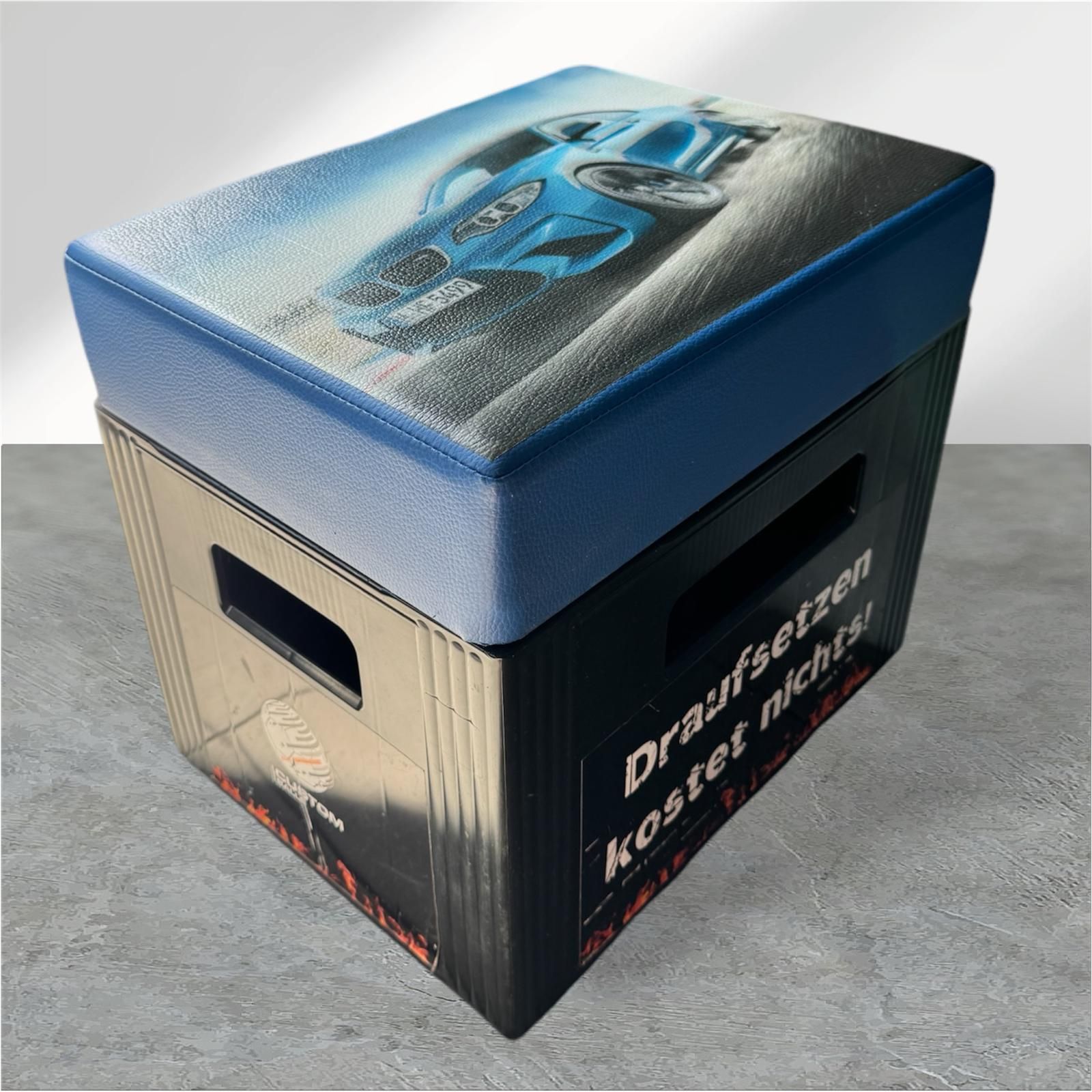 Blauer Auto-Polstersitz auf einer schwarzen Kiste mit der Aufschrift „Draufsetzen kostet nichts!“