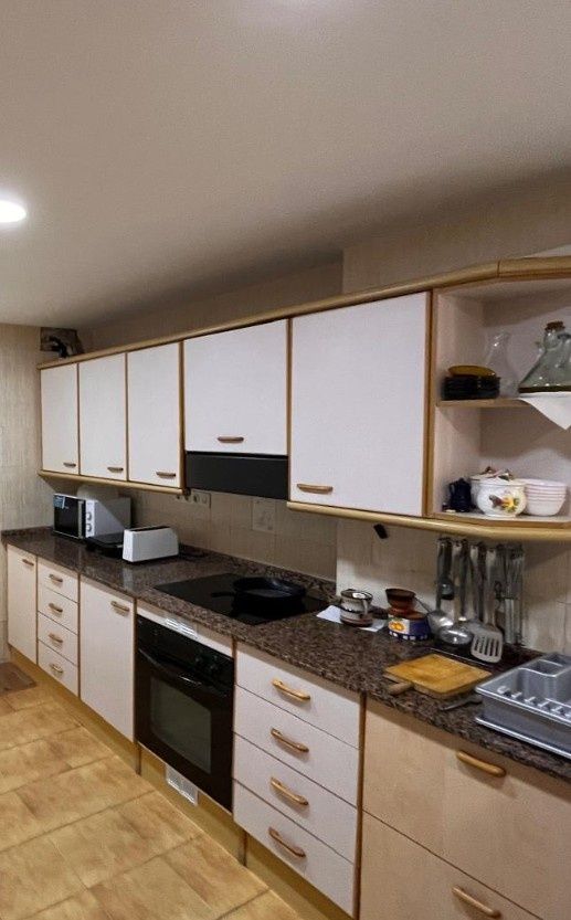 Cocina moderna con armarios blancos, encimeras negras, horno, fregadero y suelo de madera.