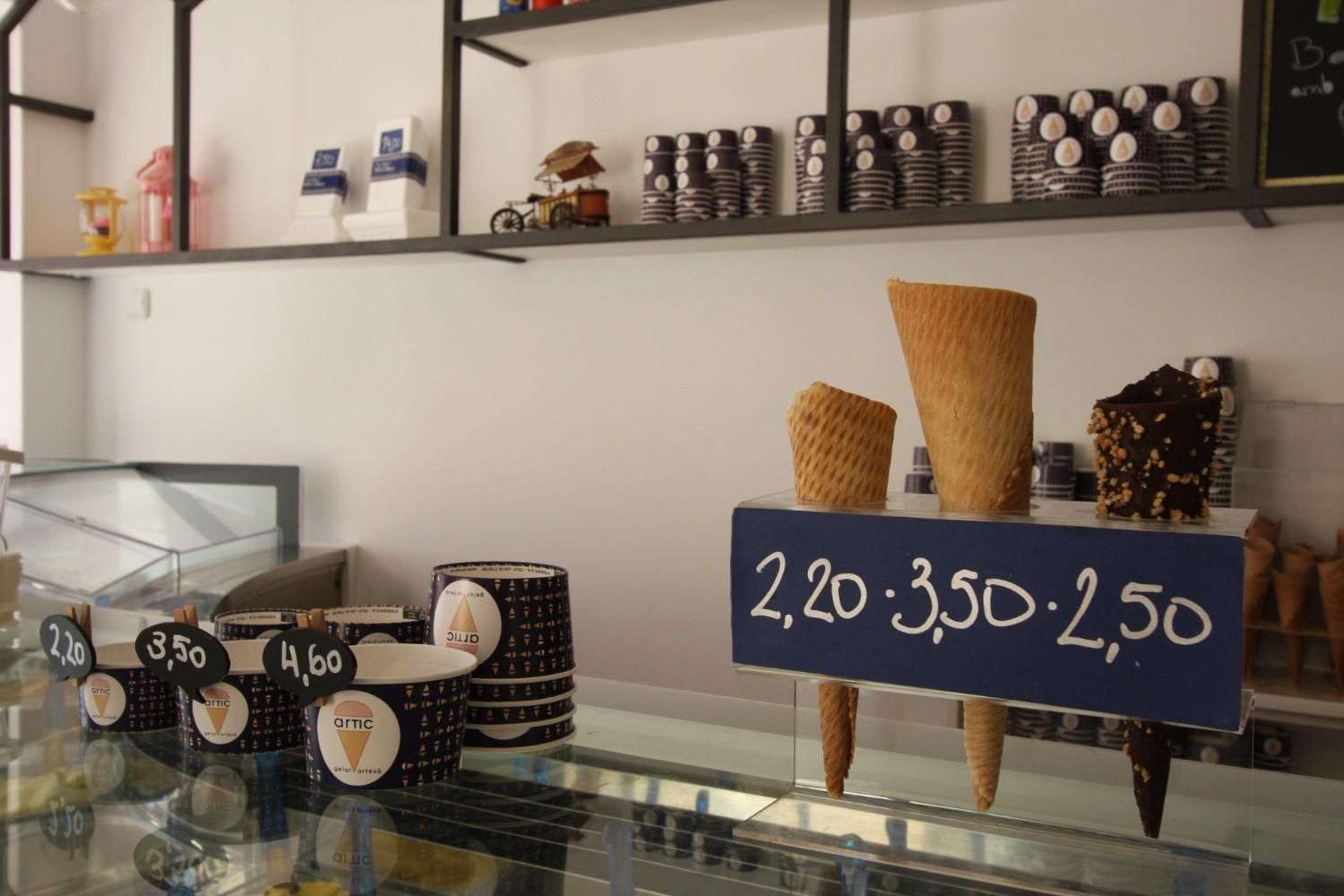 Mostrador de heladería con conos de gofre, vasos y un cartel de precios que indica 2,20 3,50 2,50