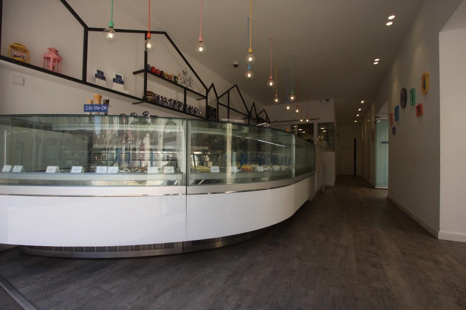 Panadería moderna vacía con vitrinas de cristal y lámparas colgantes en un interior de tienda estrecho.
