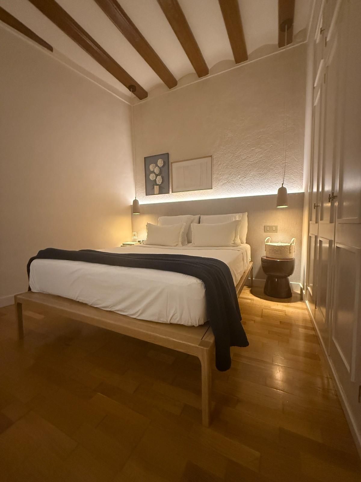 Habitación acogedora con cama de madera, sábanas blancas, luz cálida de lámpara y vigas de techo a la vista.