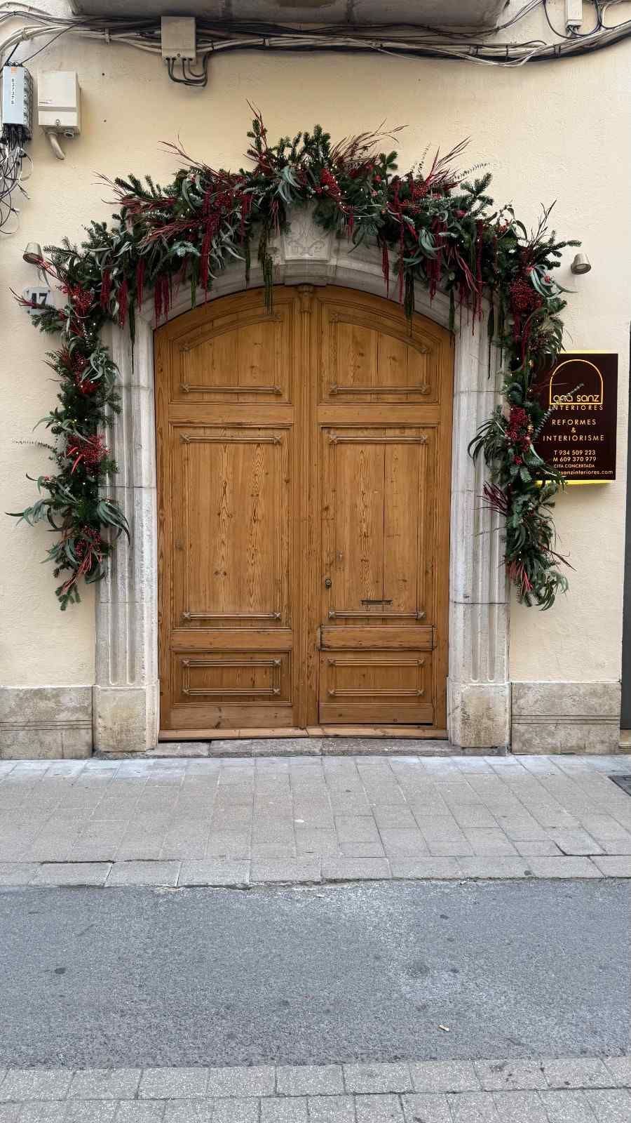 Puerta arqueada de madera con guirnalda floral en la fachada de un edificio de piedra.