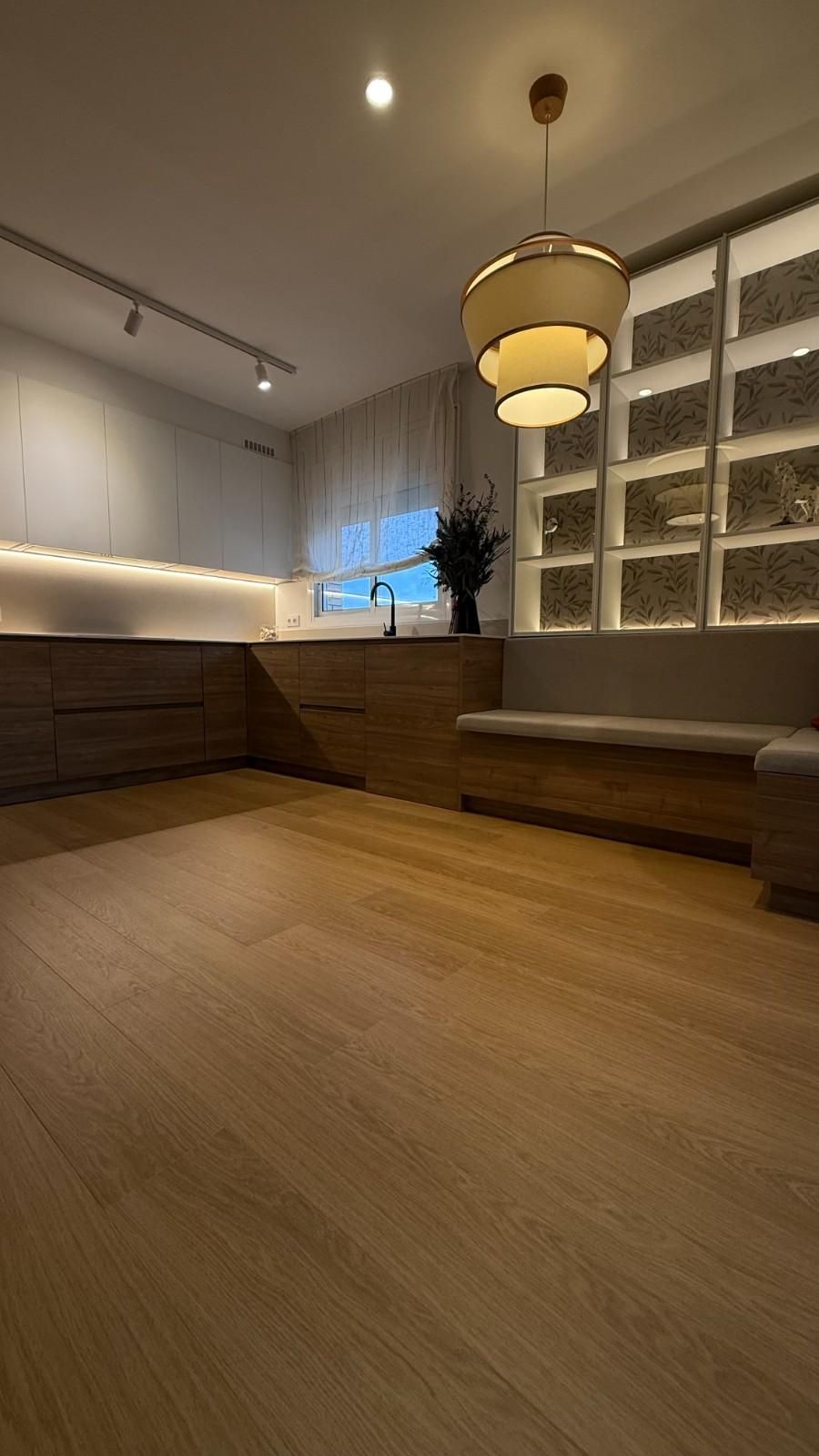Acogedor salón moderno con suelo de madera, bancos empotrados, lámparas colgantes y pared de bloques de vidrio.
