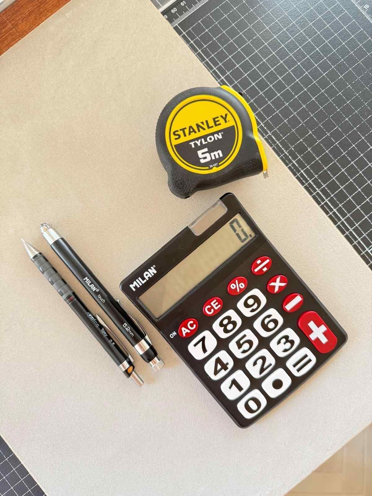 Calculadora negra, lápiz y goma de borrar sobre un escritorio de madera con un bolígrafo azul y papel al fondo.
