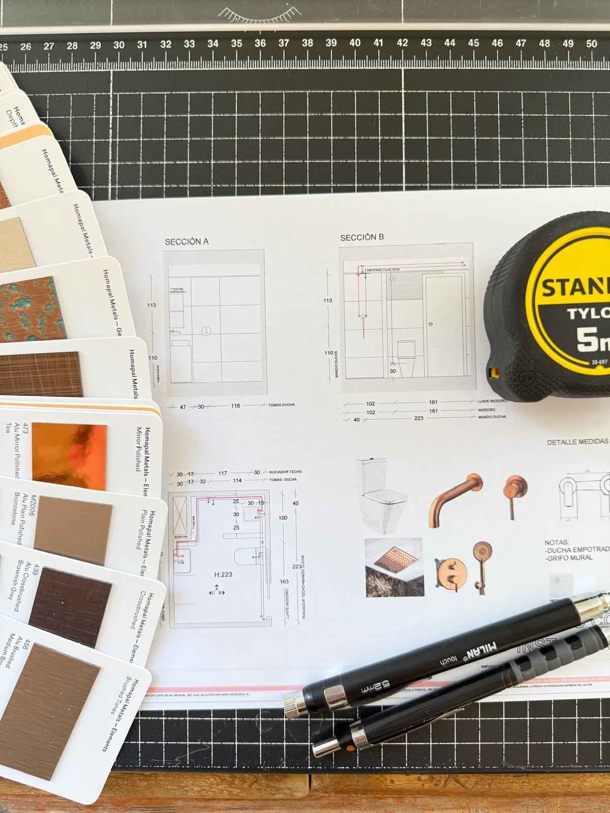 Tableta gráfica y muestras de tela/color sobre bocetos y planos de diseño en un escritorio.