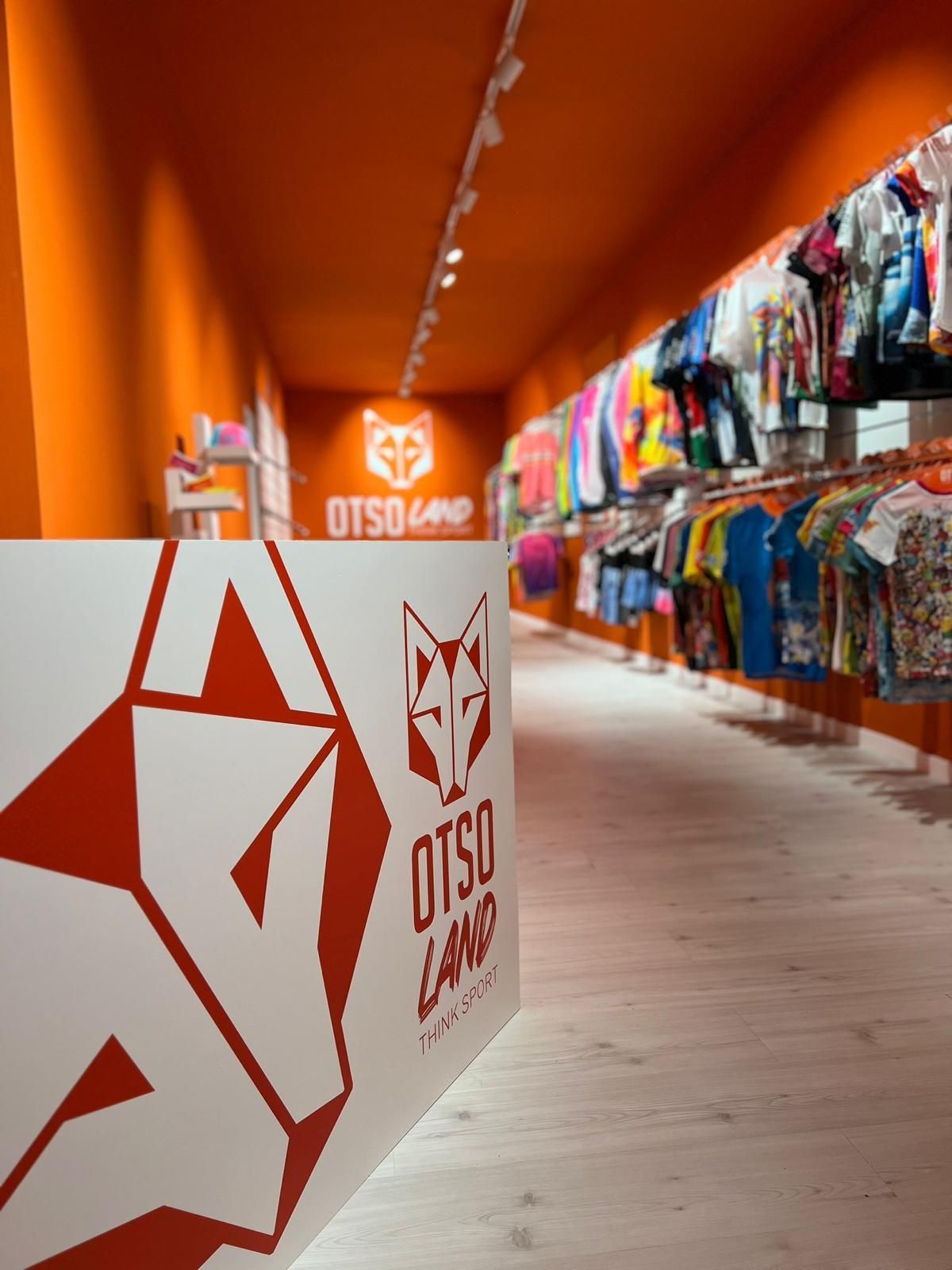 Interior de una tienda de ropa de color naranja brillante con percheros llenos de ropa colorida y un mostrador de la marca OTSO.