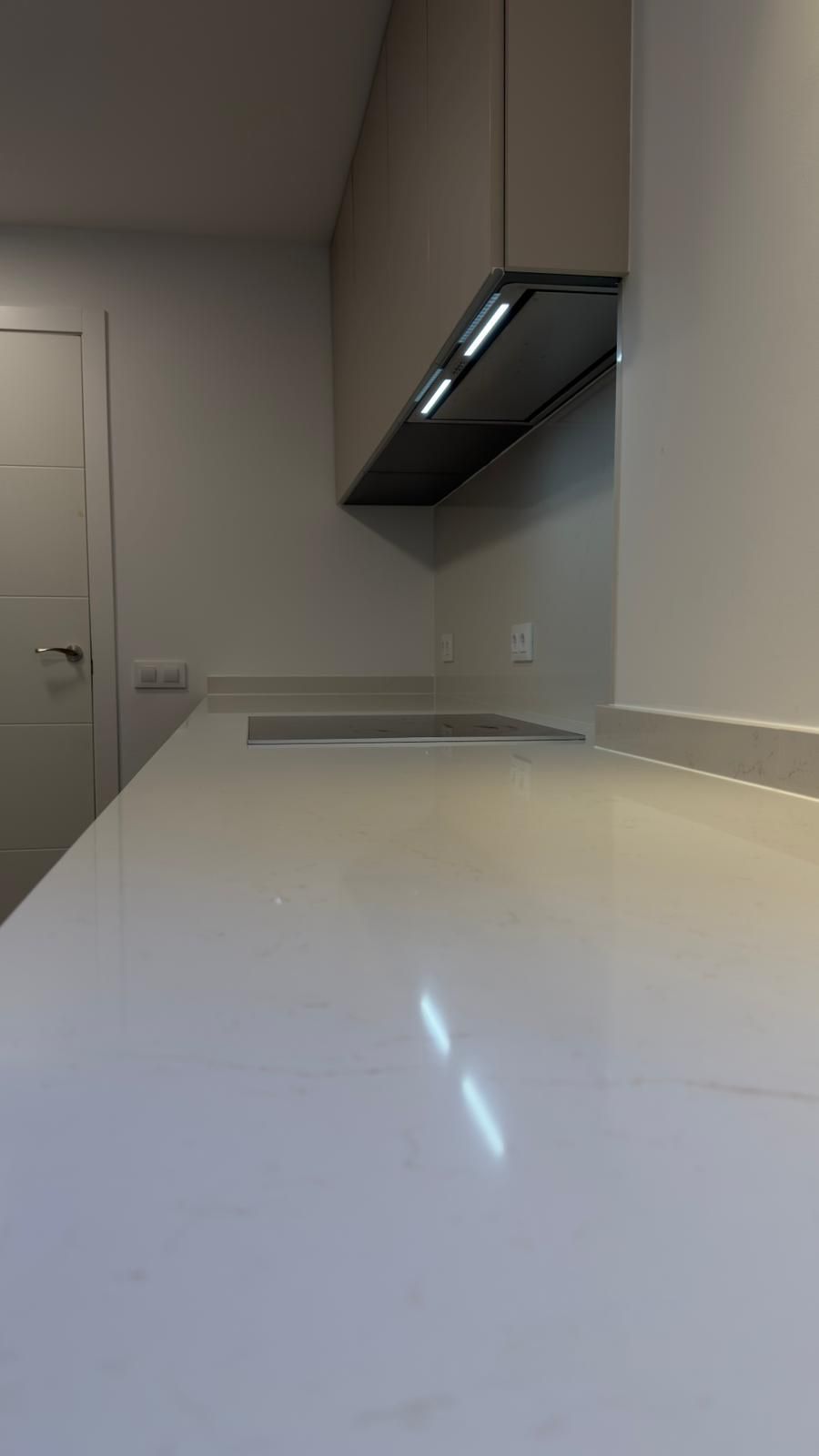 Encimera de cocina moderna con armarios blancos y campana extractora negra.