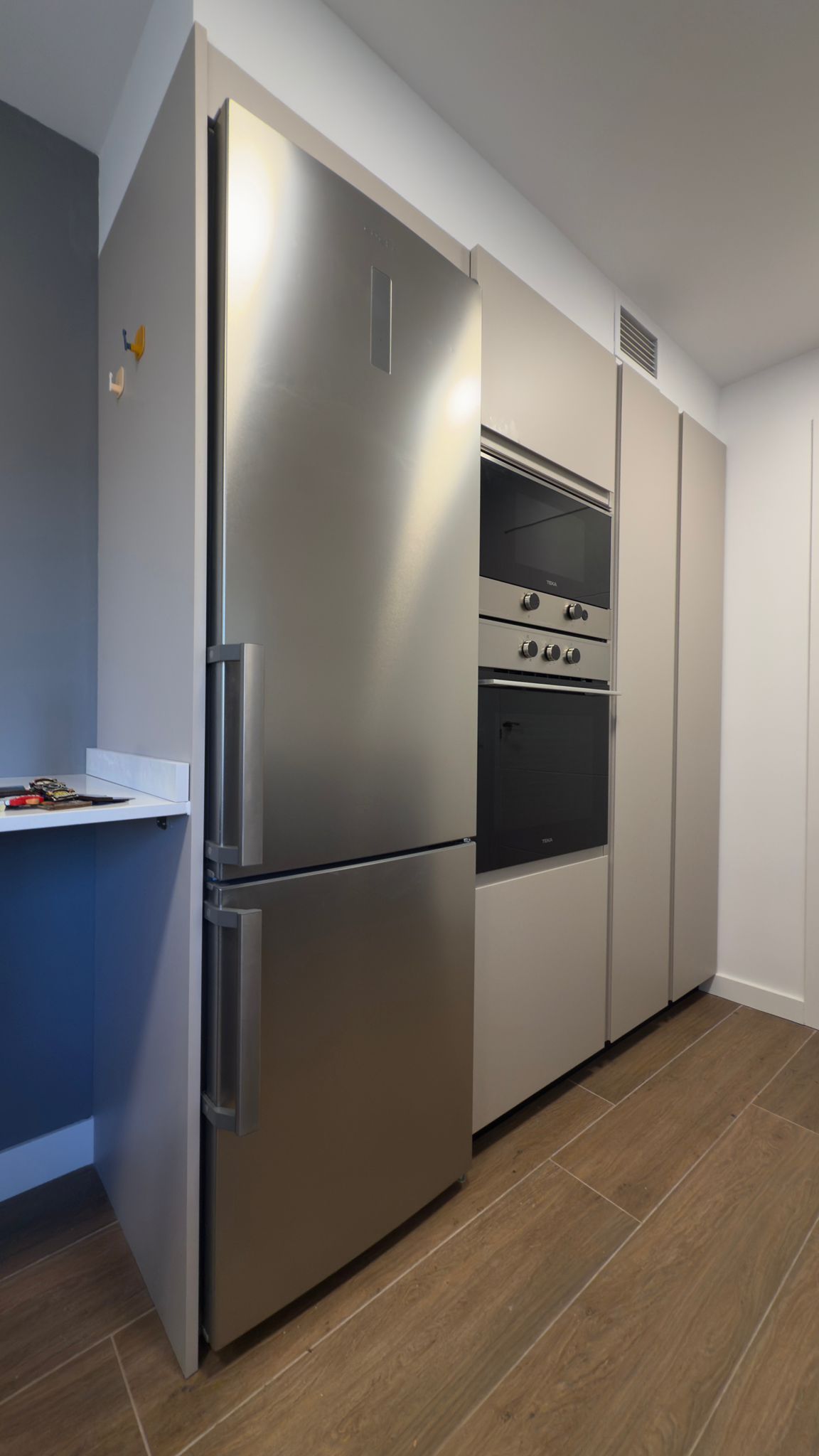 Refrigerador de acero inoxidable junto a horno empotrado y armarios en una cocina moderna.