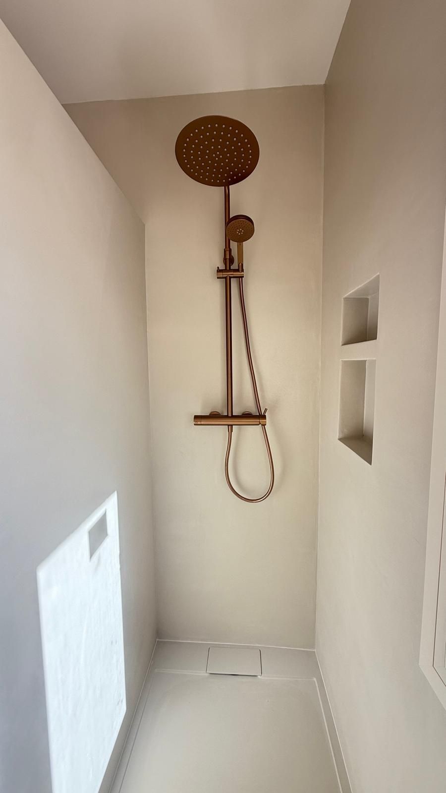 Cabina de ducha moderna con cabezal de ducha tipo lluvia montado en la pared, ducha de mano y nichos integrados en paredes blancas.