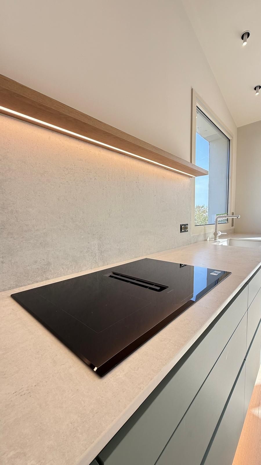 Cocina moderna minimalista con placa de cocción negra, encimeras claras e iluminación bajo los armarios.