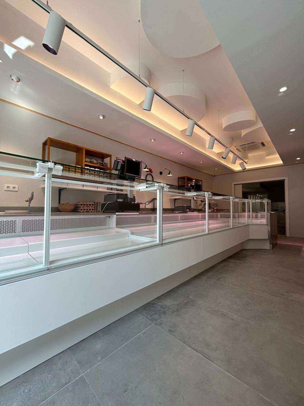 Mostrador de cafetería moderno vacío con vitrinas de cristal, molduras blancas e iluminación de riel bajo un techo curvo.