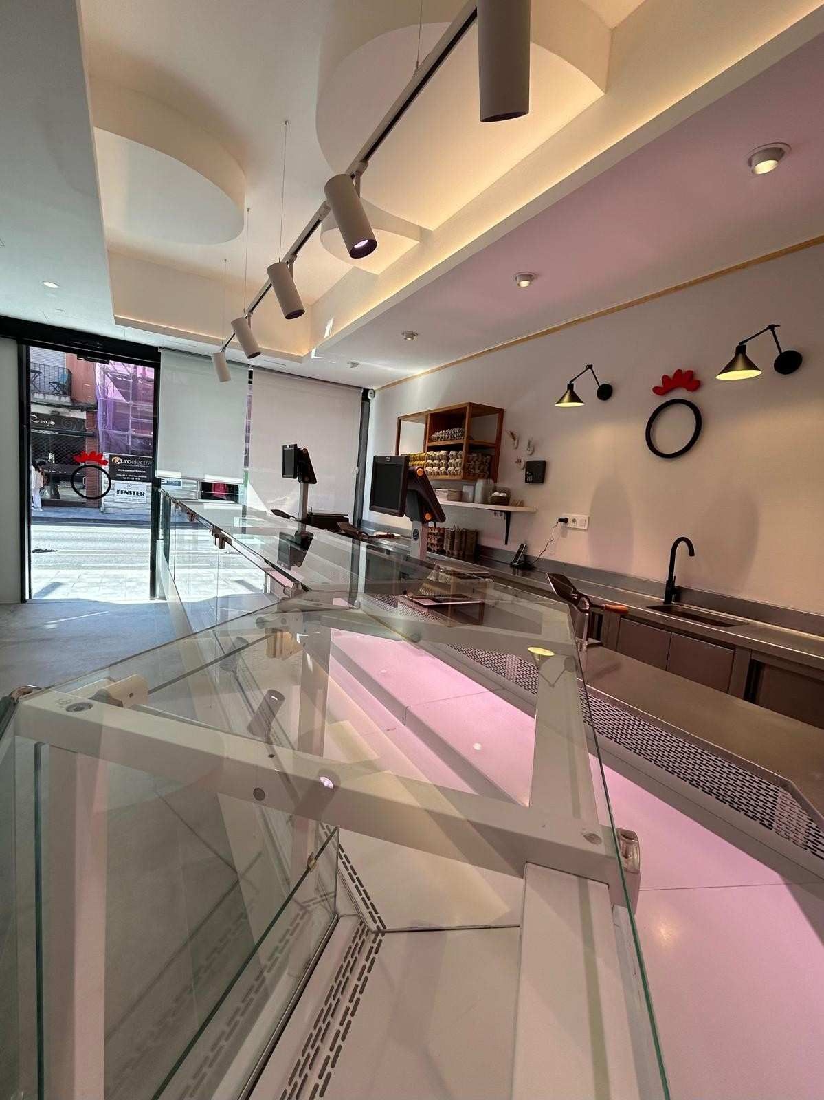 Interior de cafetería moderno con vitrinas de cristal, iluminación rosa y taburetes a lo largo de una barra.