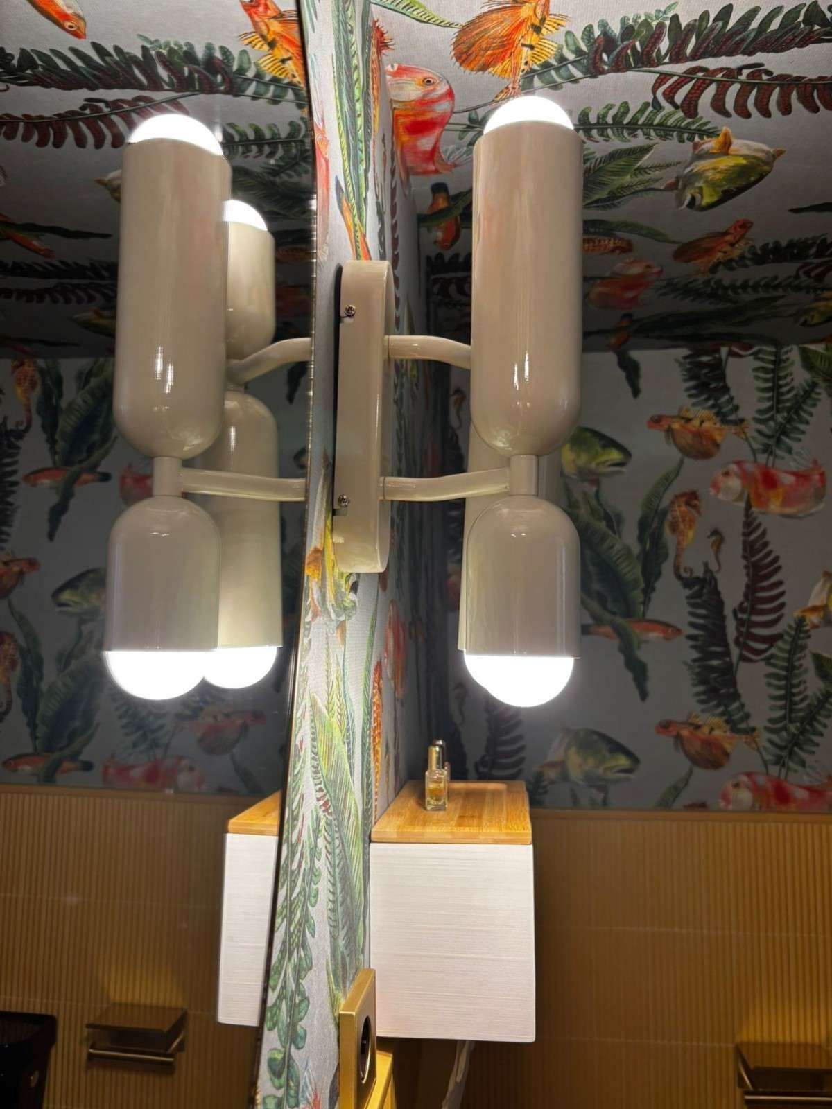 Lámpara de techo con cuatro bombillas cilíndricas blancas y baldosas de techo con estampado de peces de colores debajo.