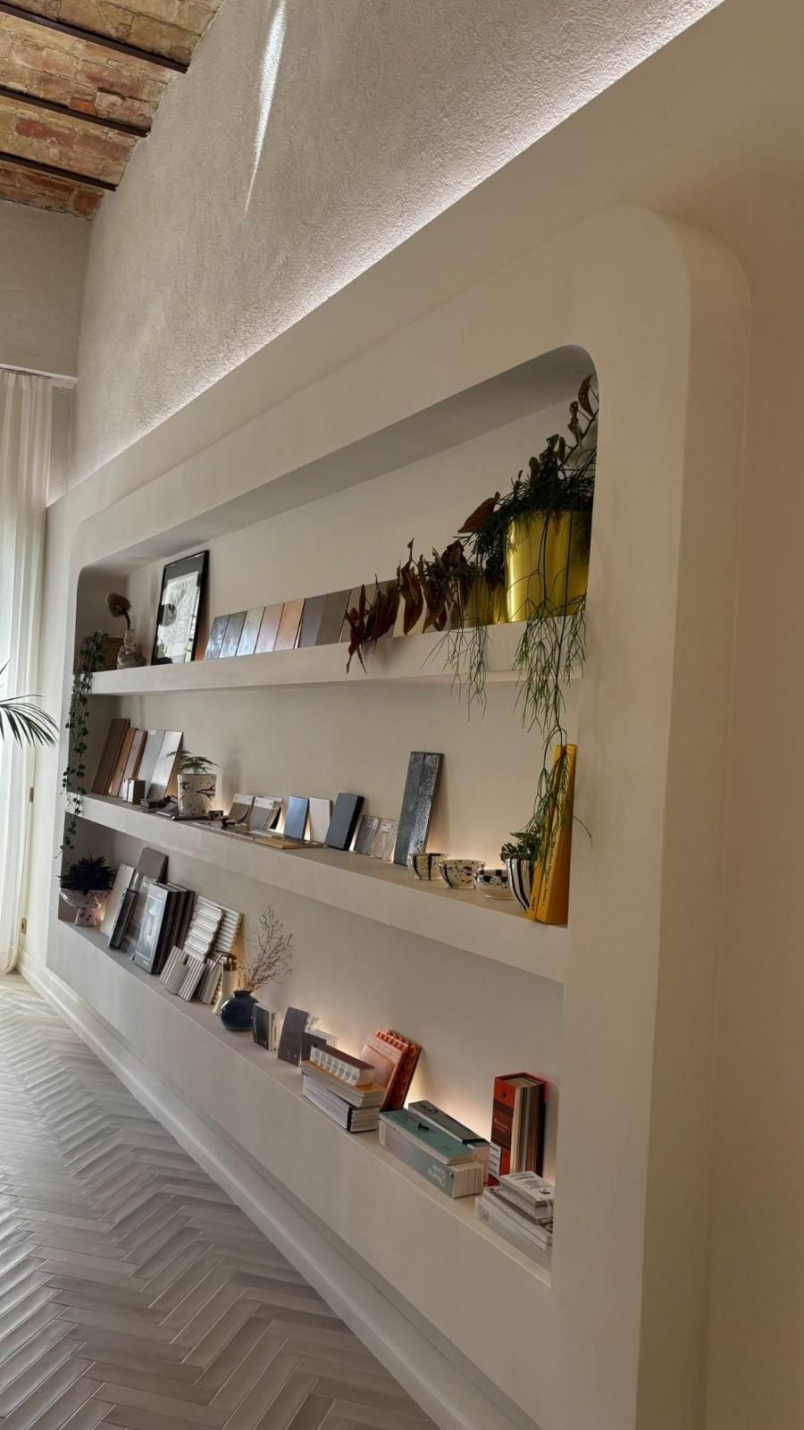 Estanterías empotradas en la pared que exhiben libros y elementos decorativos en un pasillo luminoso y minimalista.