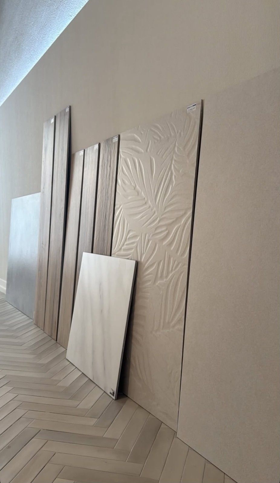 Varios paneles de madera y una pizarra blanca apoyados contra una pared beige sobre un suelo de madera en espiga.