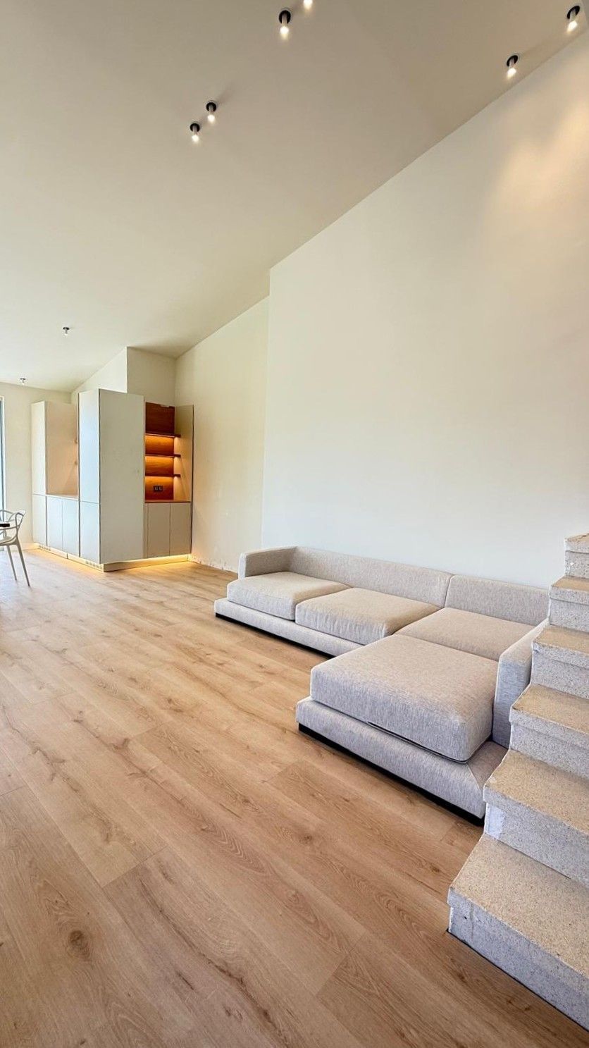 Sala de estar minimalista con pisos de madera clara, paredes blancas y sofá modular gris.