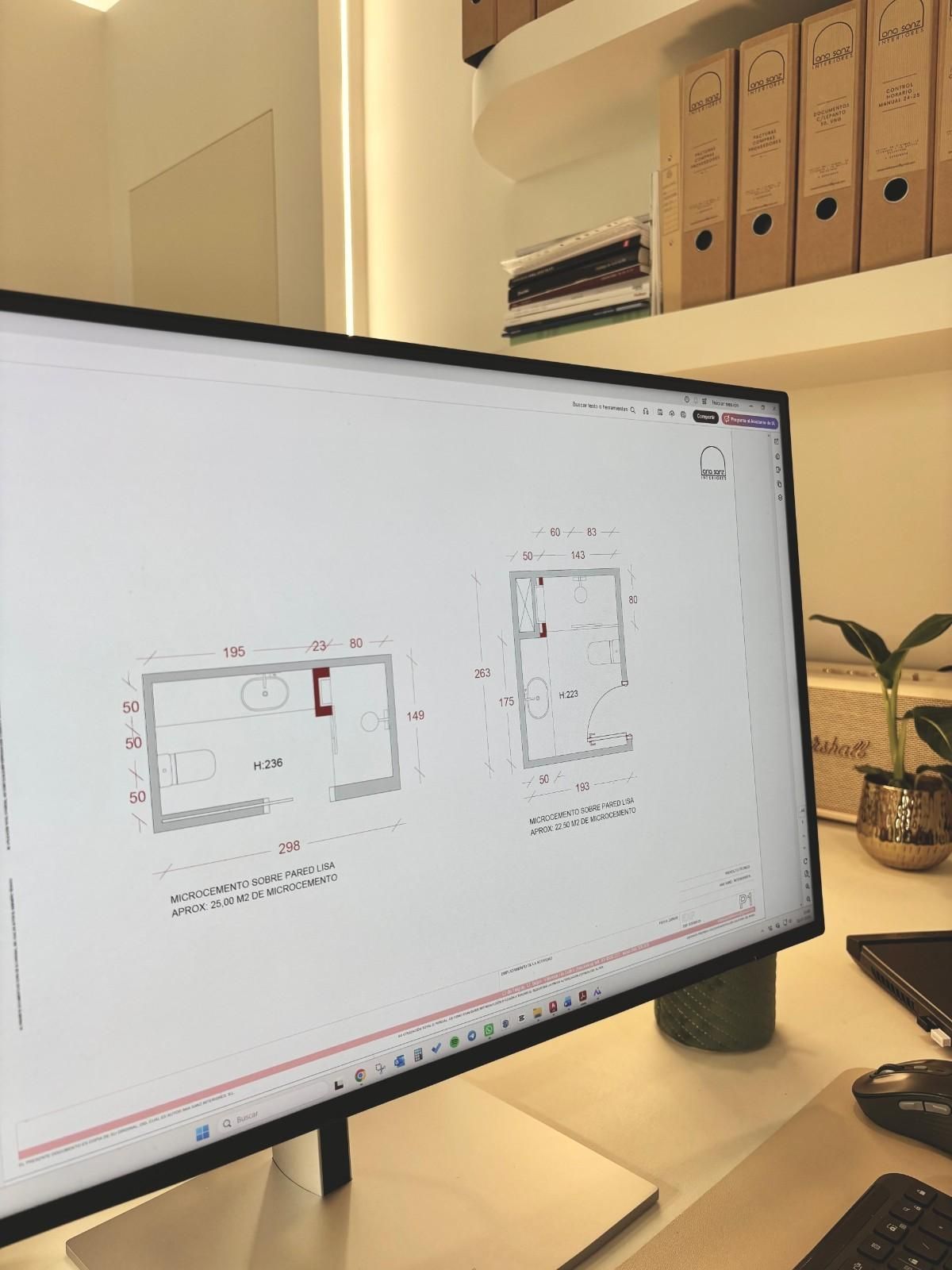 Monitor de escritorio que muestra un dibujo técnico en una oficina luminosa con carpetas en estantes cercanos.