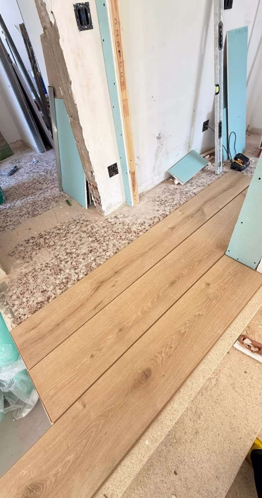 Pasillo interior en obras con paredes a la vista, escombros y nuevos paneles de suelo de madera.