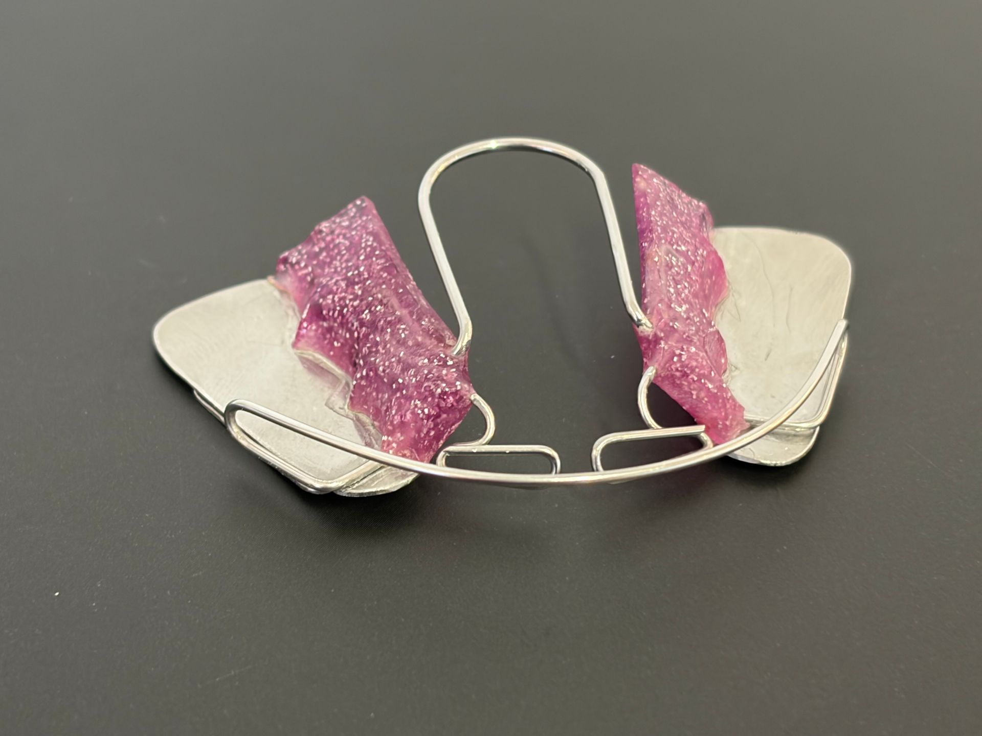 Fiocco rosa scintillante su una struttura di filo metallico bianco su sfondo grigio.