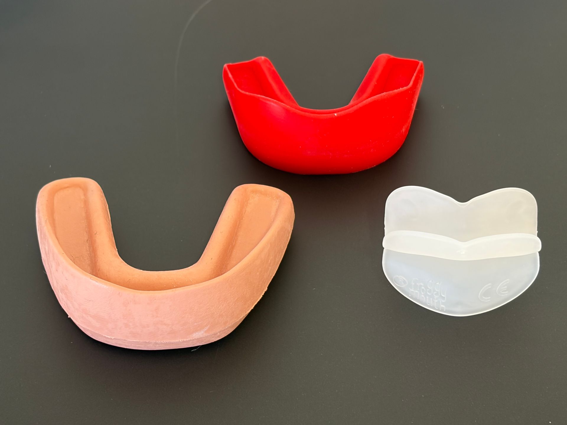 Tre paradenti dentali nei colori rosso, pesca e trasparente su sfondo scuro