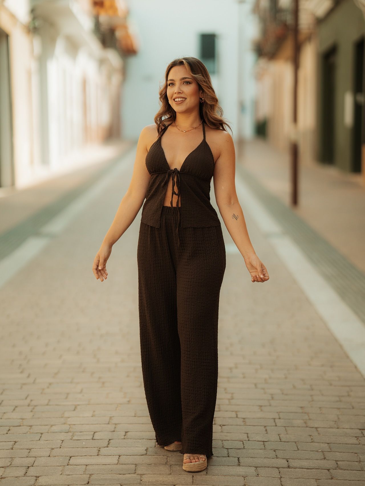 Mujer con un mono negro caminando por una calle adoquinada iluminada por el sol.