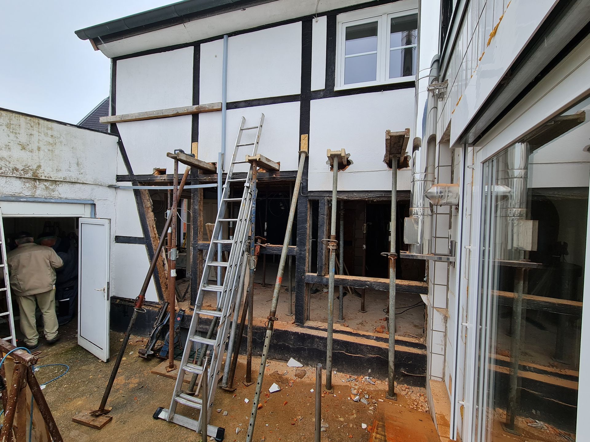 Gerüst und Leitern vor einem Haus, das renoviert wird; die Haustür ist offen und das Erdgeschoss freigelegt.