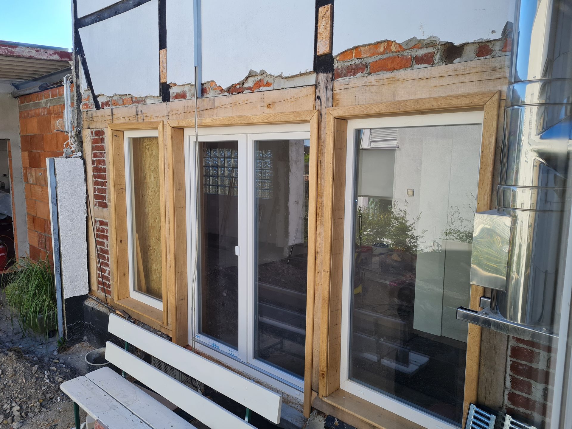 Teilweise renovierte Gebäudefassade mit großen Glasfenstern und freiliegendem Holzfachwerk