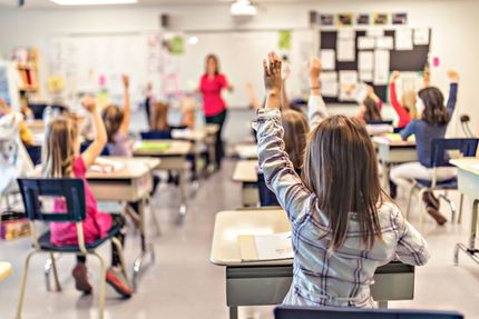 Schüler heben die Hand in einem Klassenraum