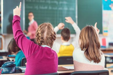 Schüler heben die Hand in einem Klassenraum