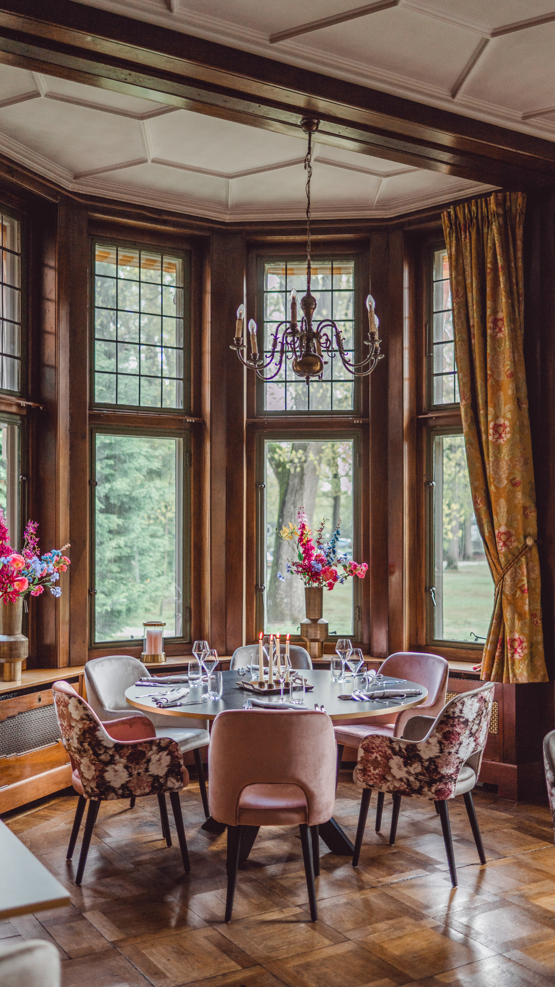Elegante eettafel gedekt voor een maaltijd, in een kamer met donkerhouten lambrisering en bloemendecoraties.