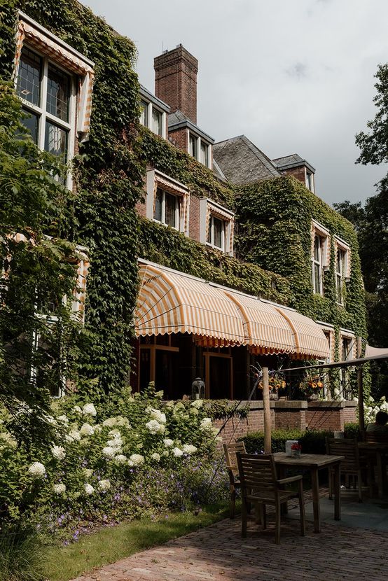 Met klimop begroeid bakstenen gebouw met een gele luifel en een terras.