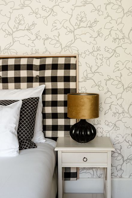 Slaapkamer met een bed met een zwart-wit geruit hoofdeinde. Een wit nachtkastje staat vol met een zwarte lamp met een gouden kap. De muur heeft een spikkelpatroon.