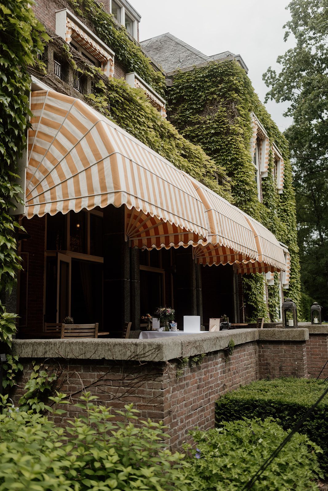 Een bakstenen gebouw met een gestreepte luifel boven een met klimop begroeid terras.