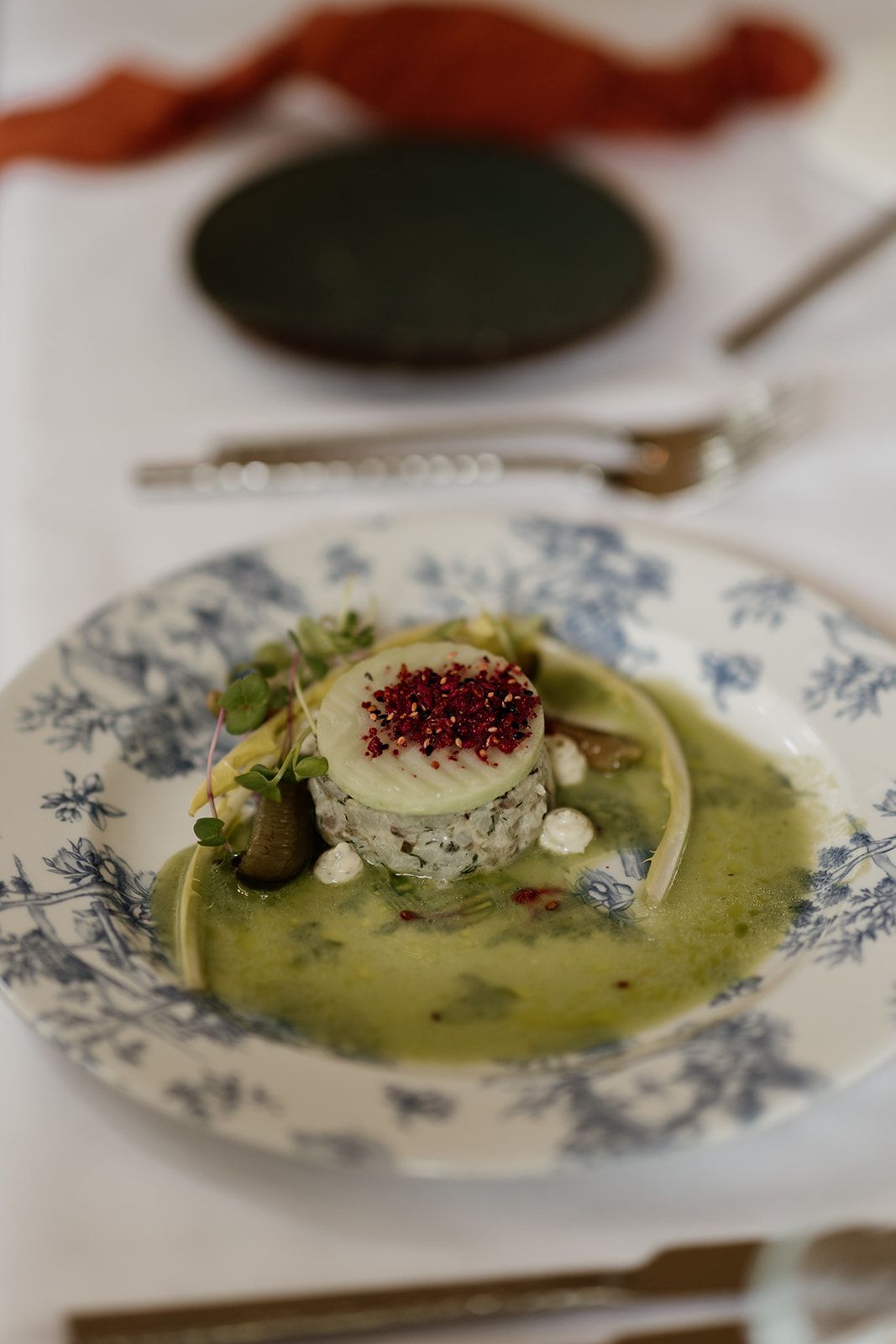 Een mooi bord met eten, groene saus, een cilinder met een witte en rode bovenkant en een blauw en wit bloemenbord.