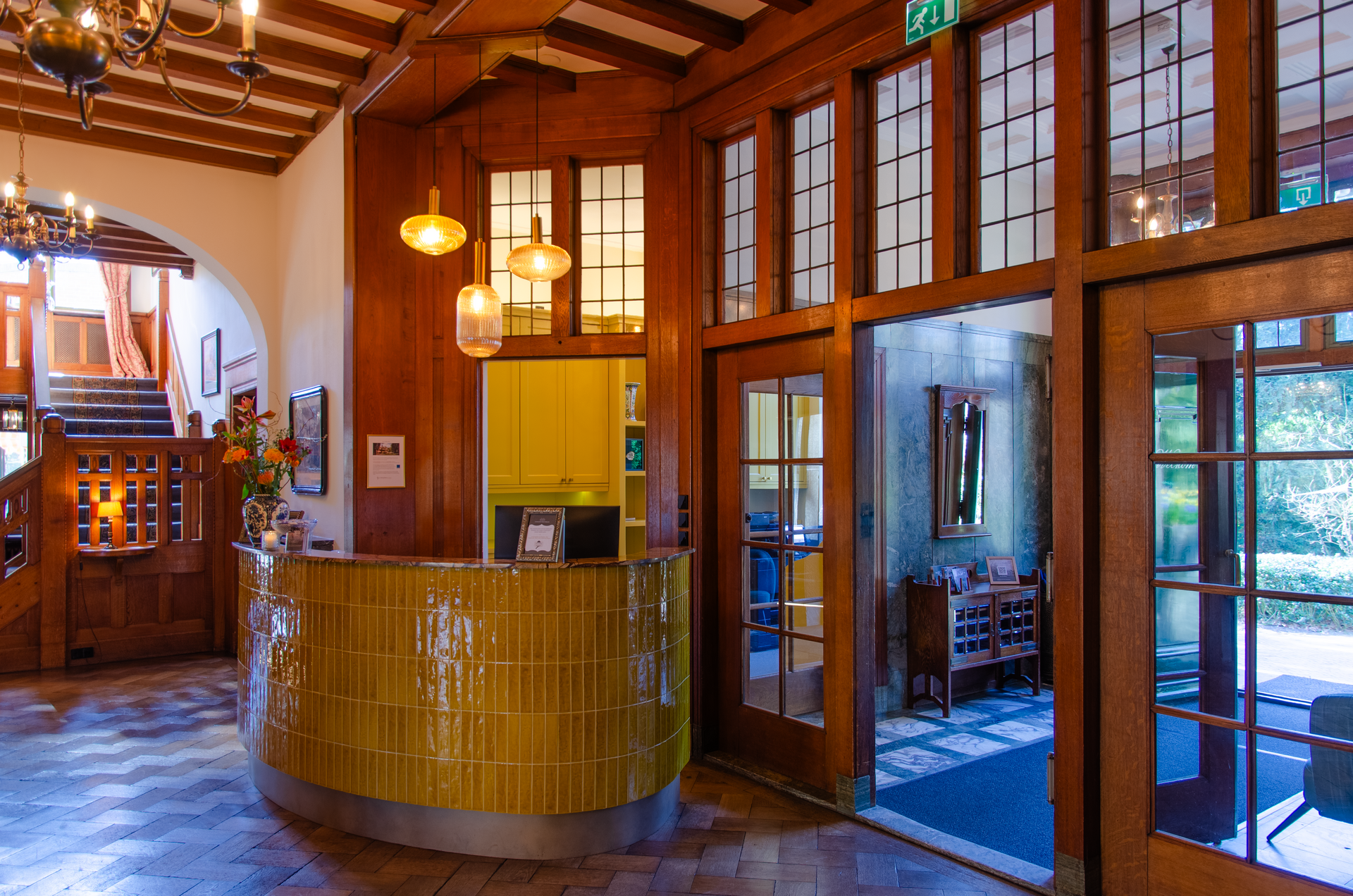 Receptie in een lobby met houten lambrisering, een gebogen deur, een trap en toegang tot een buitenruimte.
