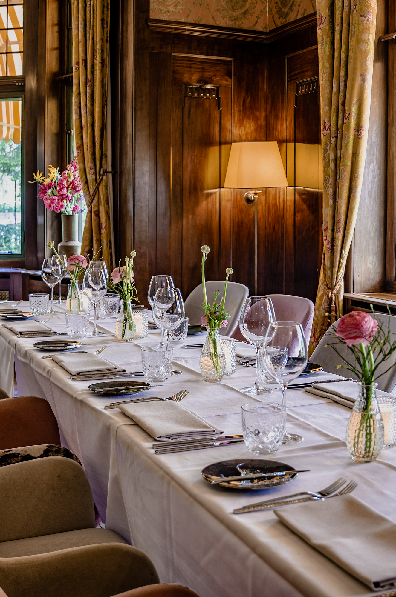Elegante eettafel gedekt voor een maaltijd, in een kamer met donkerhouten lambrisering en bloemendecoraties.