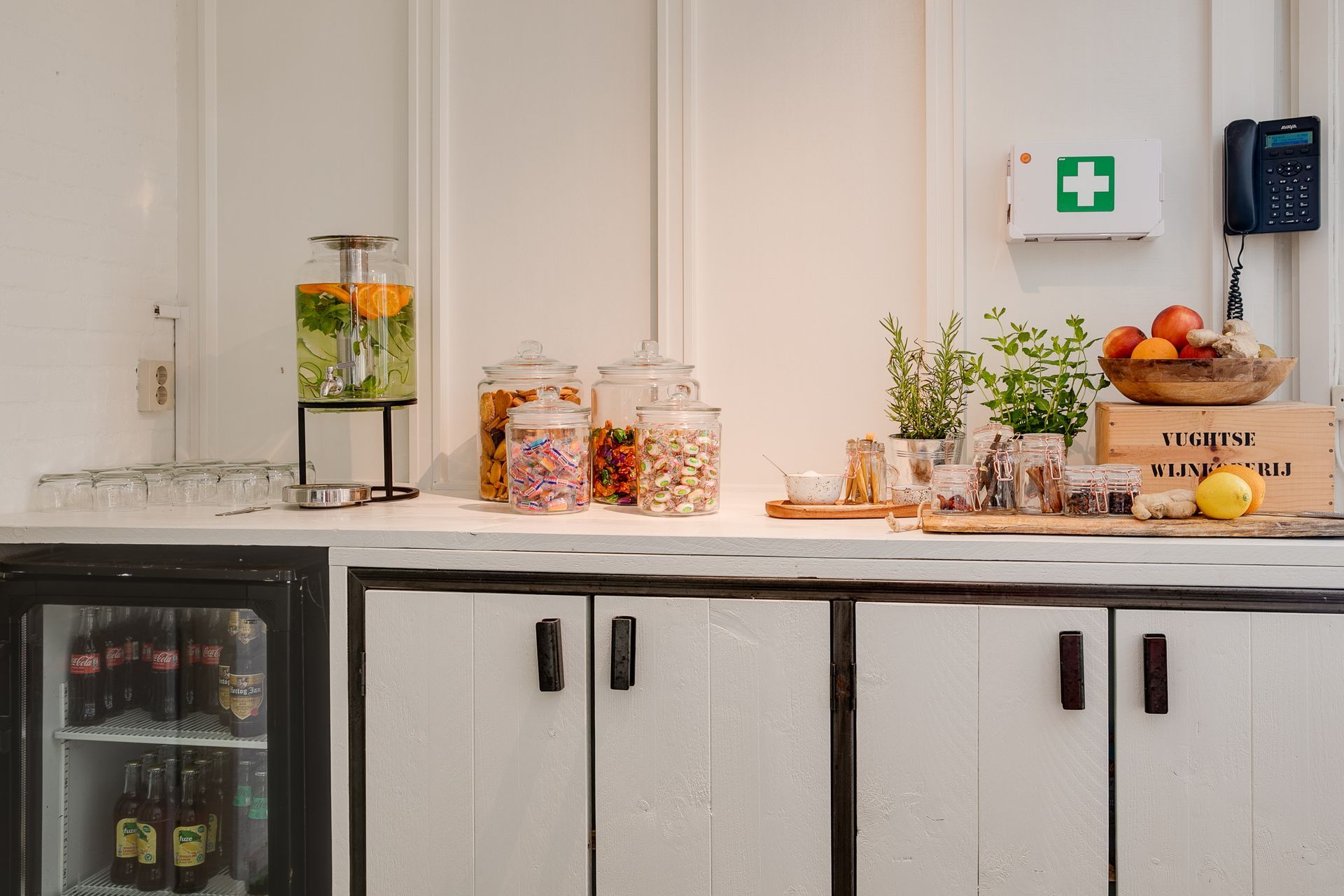 Een snackbar met een drankautomaat, potten snoep, fruit en een koelkastje tegen een witte achtergrond.