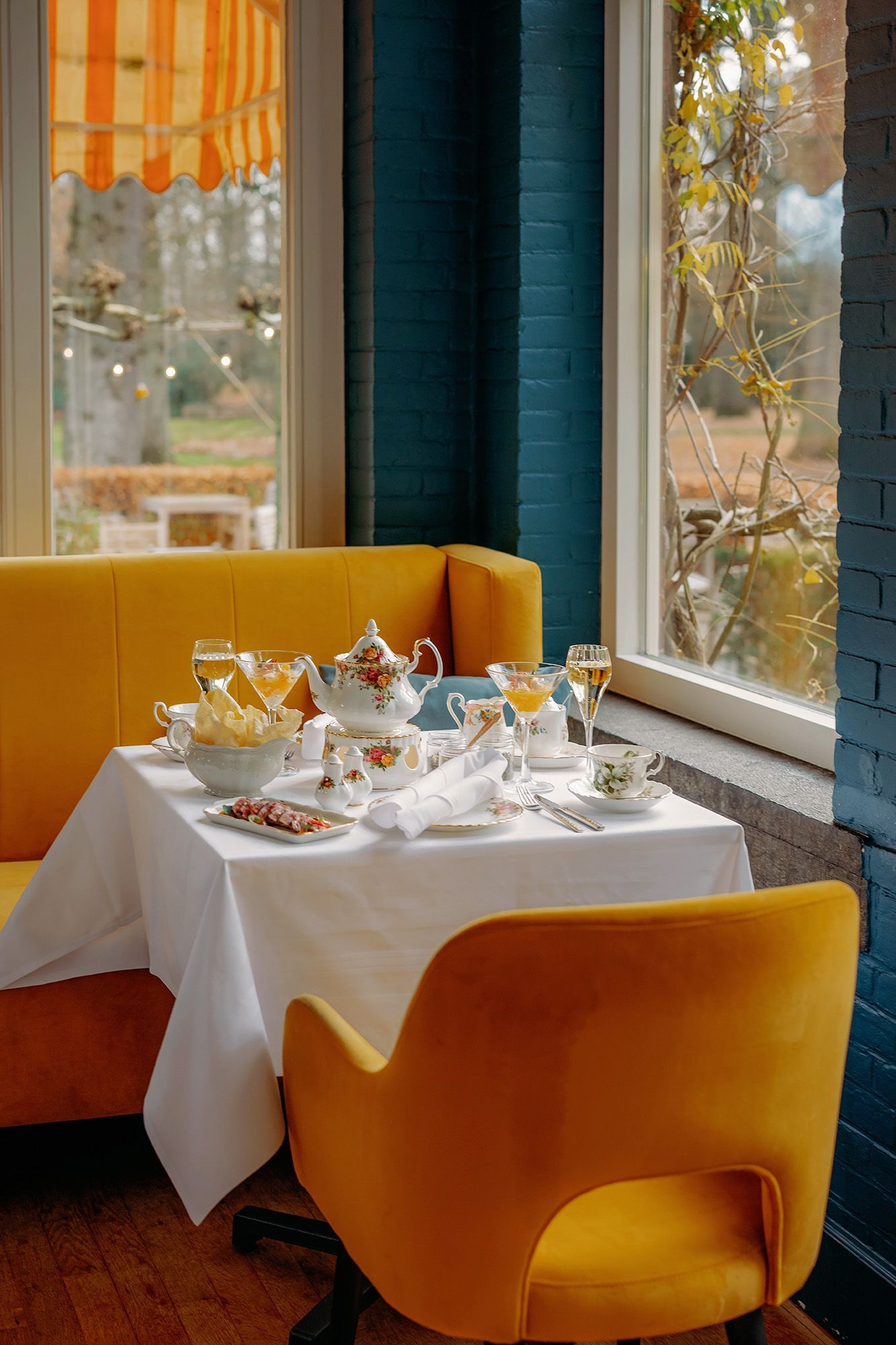 Een rijkelijk gedecoreerde eetkamer met een erker, een kroonluchter en gedekte tafels voor een maaltijd. Rode en gouden accenten domineren de ruimte.