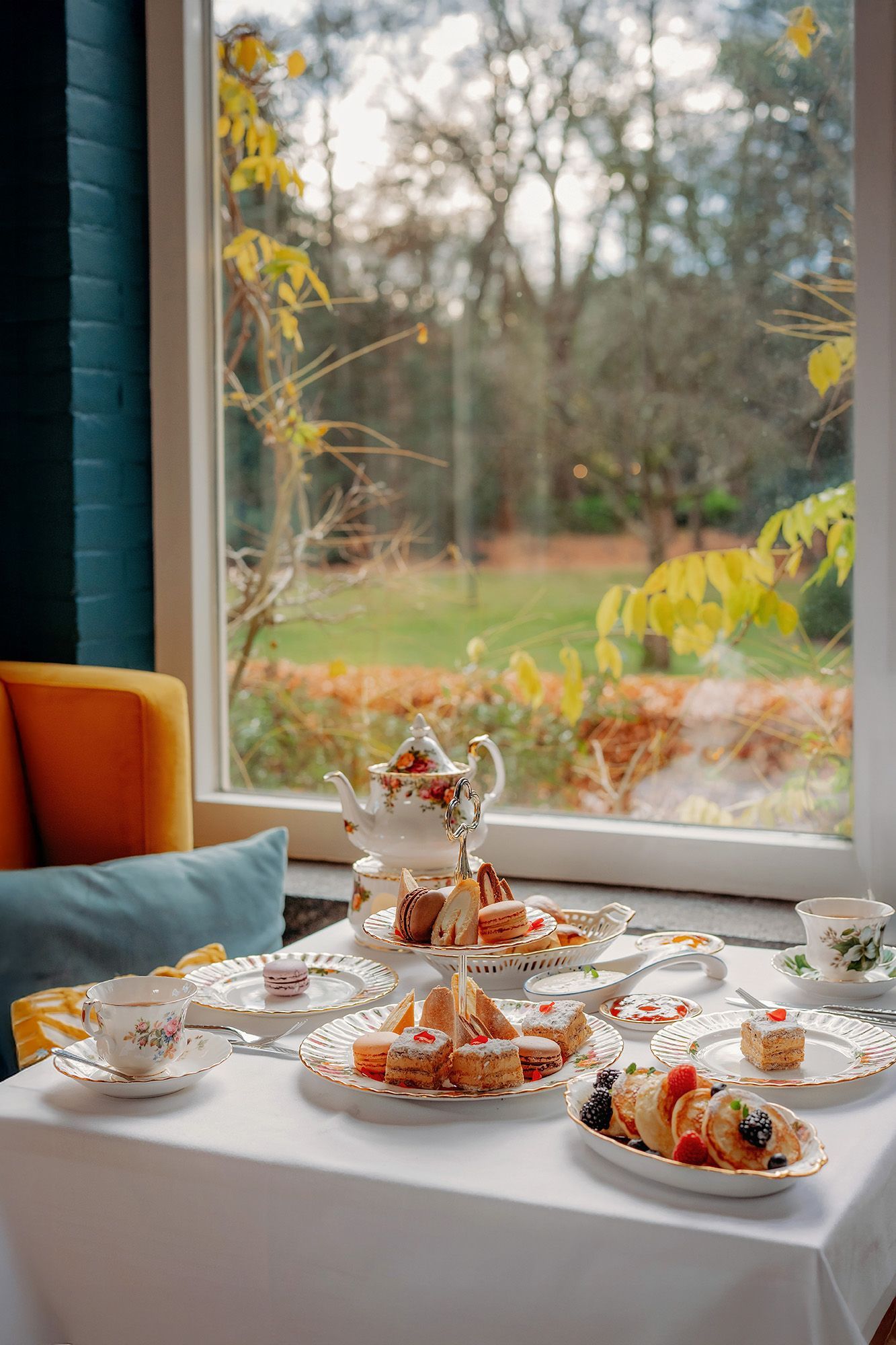 Een ober draagt twee borden met eten op een terras. Hij draagt een lichtblauw overhemd en een donker schort en lacht naar de camera.