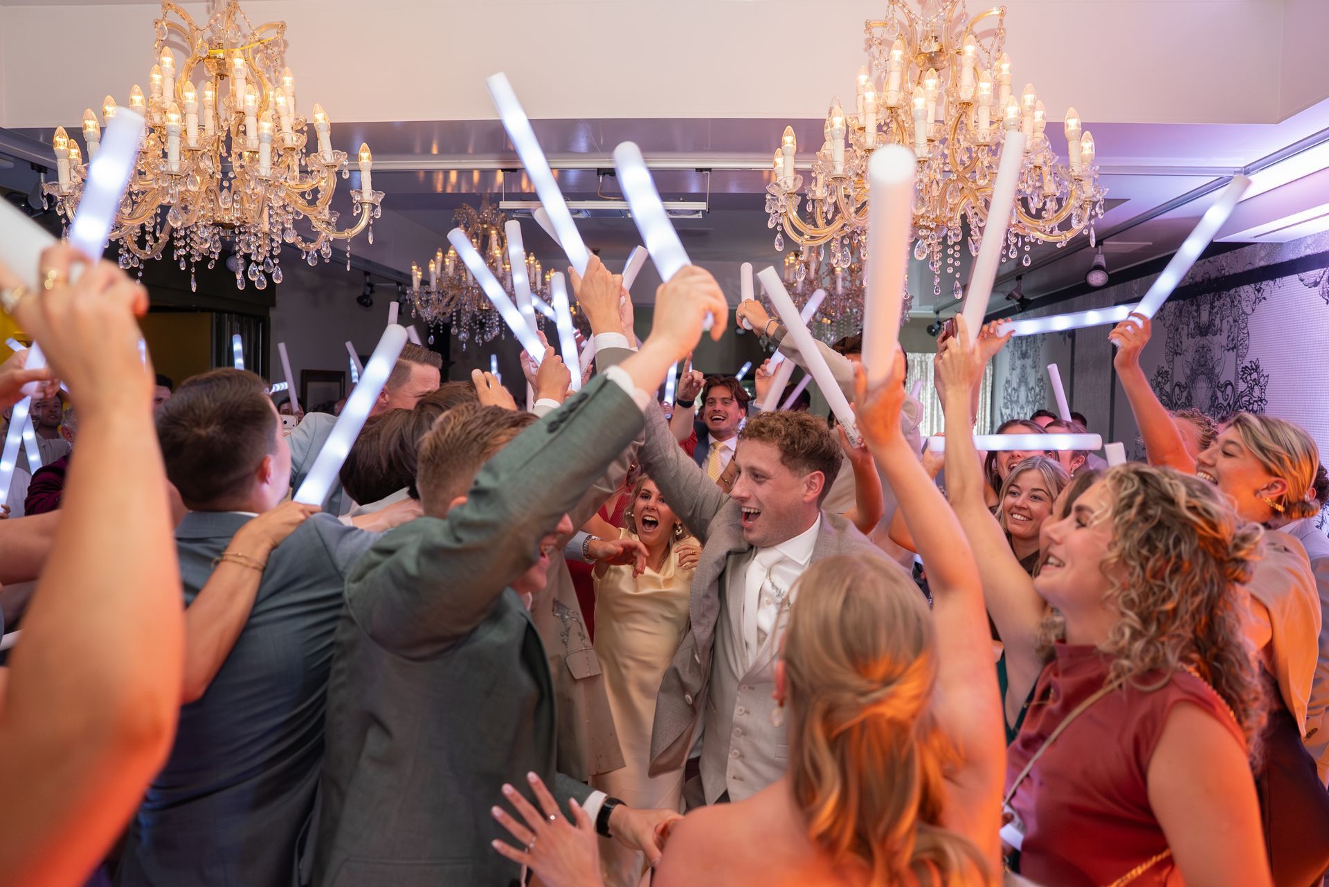 Een barman staat achter een donkerhouten bar in een sfeervol verlichte lounge, met een glas in zijn hand.